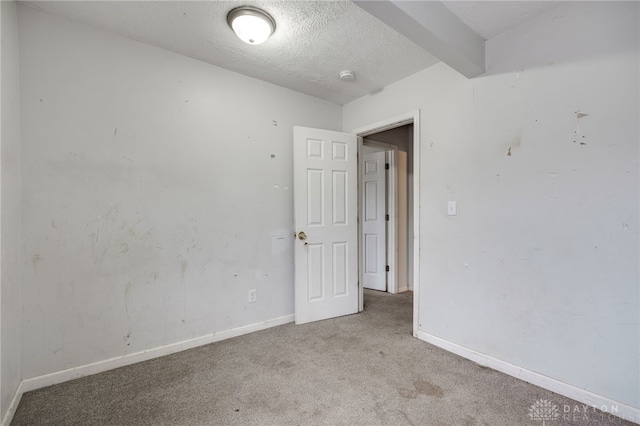 unfurnished room featuring a textured ceiling, light colored carpet, and beamed ceiling