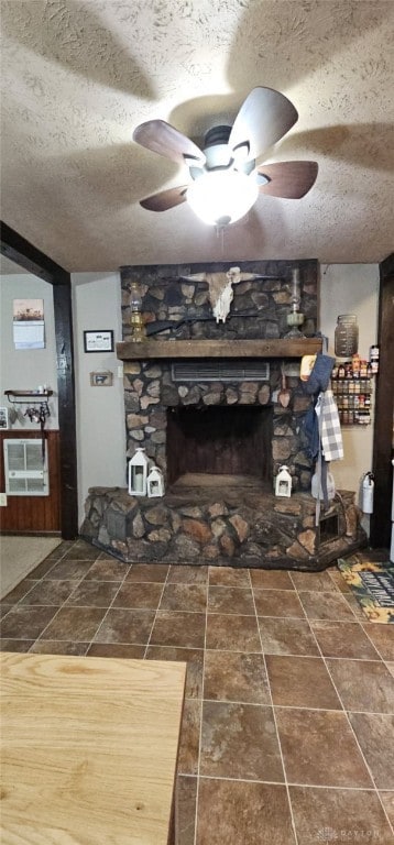 living area with stone finish flooring, ceiling fan, a textured ceiling, and a fireplace