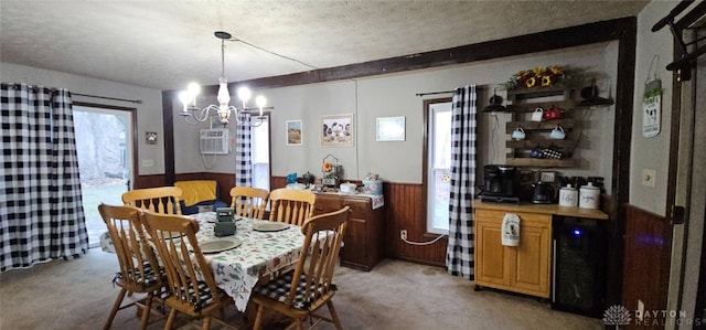 carpeted dining room with an inviting chandelier, a healthy amount of sunlight, wooden walls, and a textured ceiling