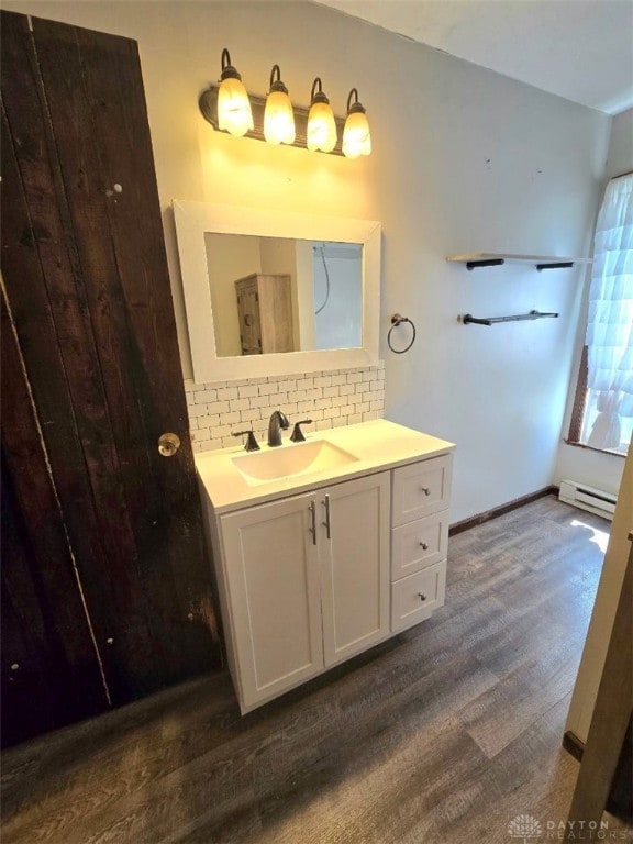 bathroom featuring a baseboard heating unit, vanity, wood finished floors, and decorative backsplash