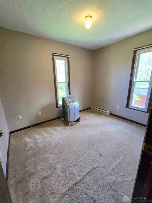 empty room featuring plenty of natural light, baseboards, a baseboard heating unit, and carpet floors