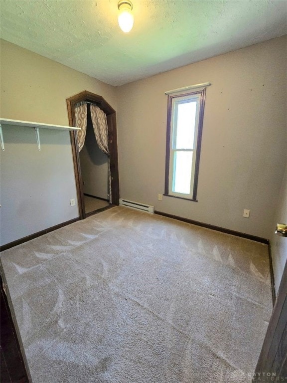 carpeted empty room featuring a baseboard heating unit and baseboards