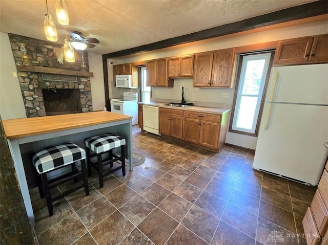 kitchen featuring a textured ceiling, a sink, brown cabinetry, and white appliances