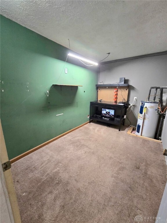 basement featuring a textured ceiling, water heater, carpet, and baseboards