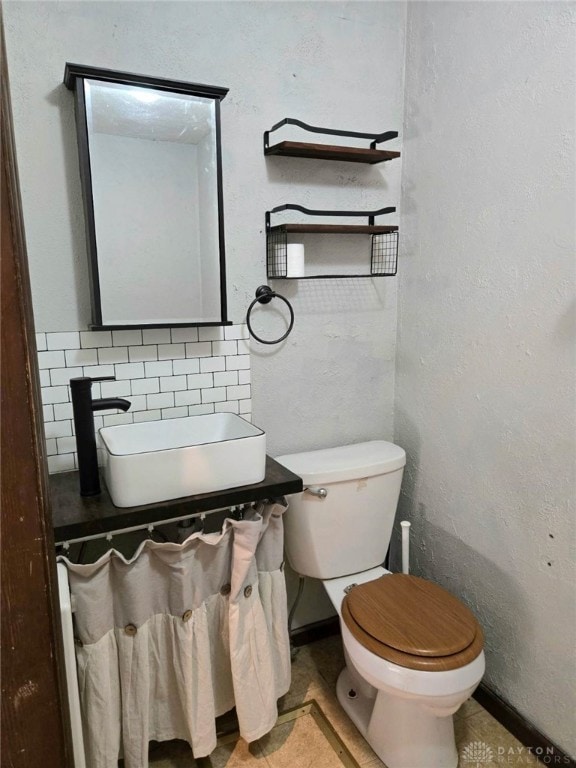 half bath with baseboards, toilet, decorative backsplash, and a sink