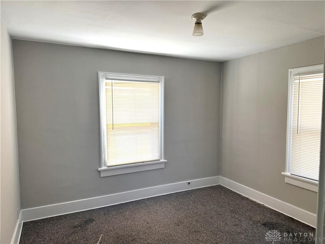 empty room with baseboards, dark colored carpet, and a wealth of natural light