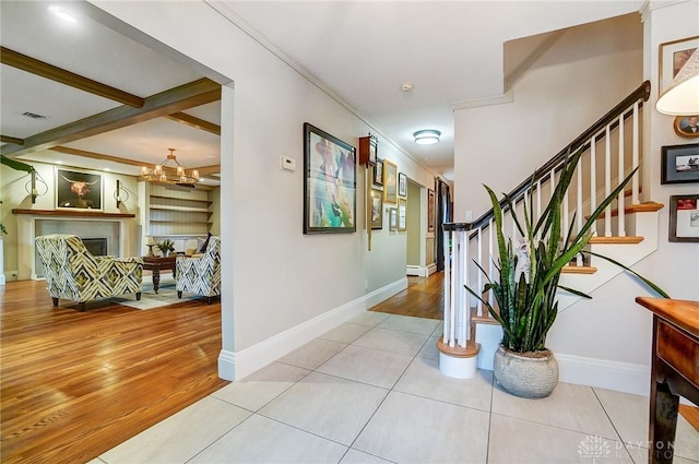 hallway with beam ceiling, ornamental molding, an inviting chandelier, and light tile patterned floors