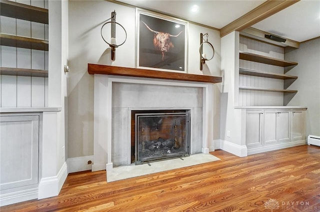 unfurnished living room with beamed ceiling, light hardwood / wood-style floors, built in shelves, and a baseboard heating unit