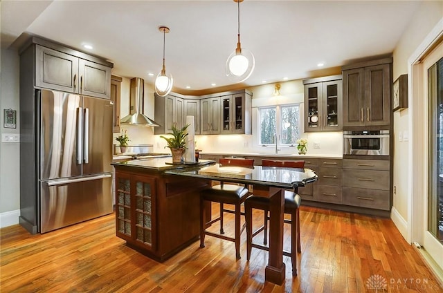 kitchen featuring appliances with stainless steel finishes, a kitchen bar, a center island, wall chimney exhaust hood, and dark brown cabinets