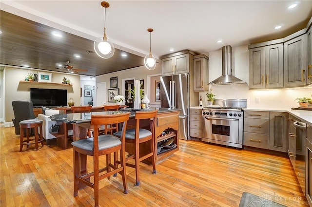 kitchen with decorative light fixtures, light wood-type flooring, high quality appliances, and wall chimney range hood