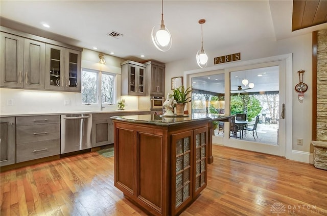 kitchen with light wood-type flooring, stainless steel dishwasher, dark stone countertops, and hanging light fixtures