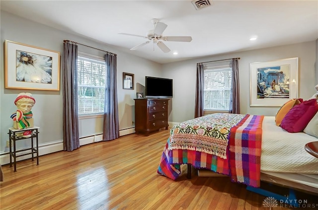 bedroom with multiple windows, light hardwood / wood-style flooring, ceiling fan, and a baseboard heating unit