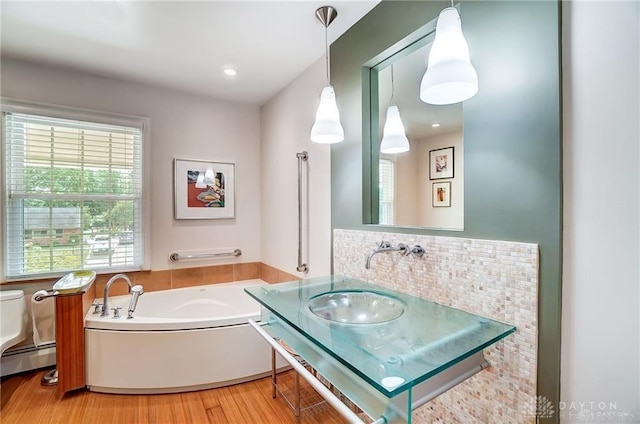 bathroom with wood-type flooring, sink, backsplash, a tub, and baseboard heating