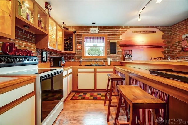 kitchen featuring brick wall, white electric stove, tasteful backsplash, sink, and light wood-type flooring