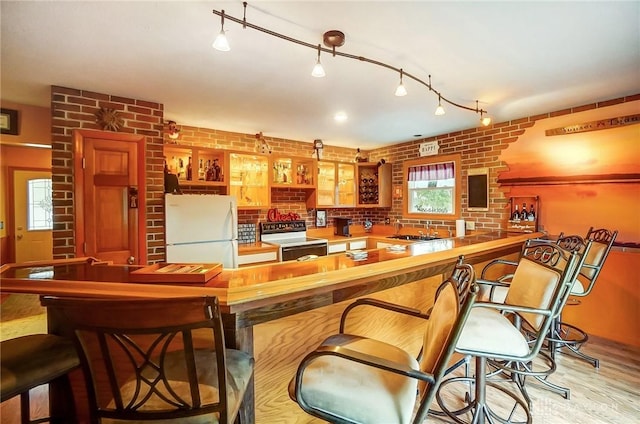 bar with sink, light hardwood / wood-style flooring, electric range, white refrigerator, and brick wall