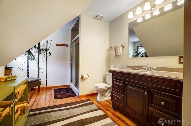 bathroom featuring wood-type flooring, toilet, a shower with shower door, and vanity