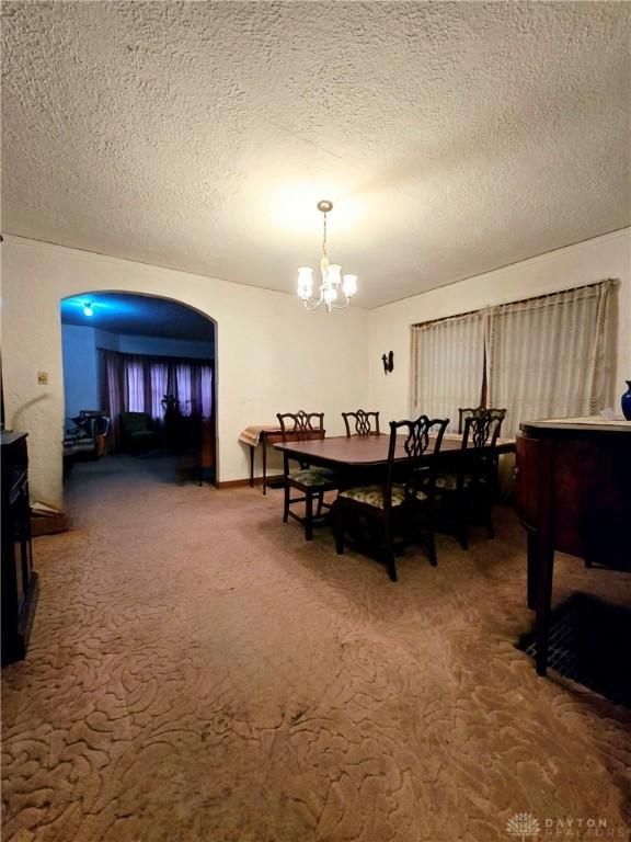 dining space featuring a textured ceiling, carpet flooring, and a chandelier