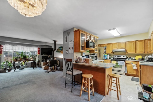 kitchen featuring a breakfast bar area, an inviting chandelier, stainless steel appliances, a wood stove, and kitchen peninsula