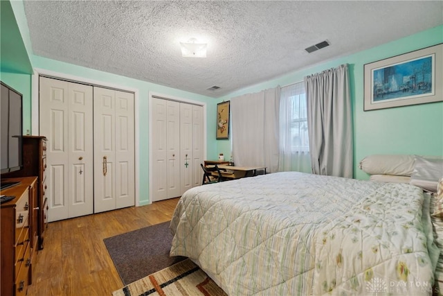 bedroom featuring two closets, a textured ceiling, and light hardwood / wood-style flooring