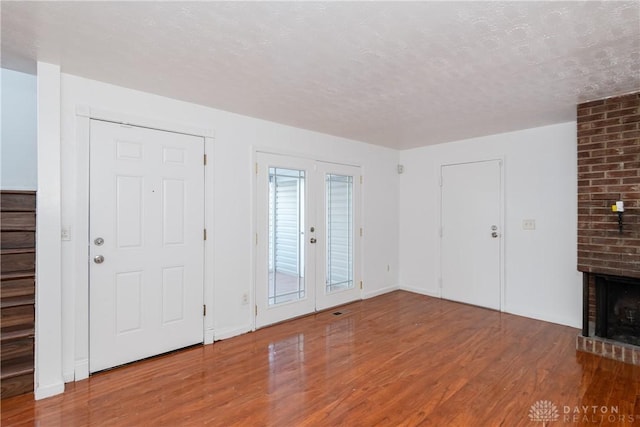 unfurnished living room with a fireplace, french doors, hardwood / wood-style floors, and a textured ceiling