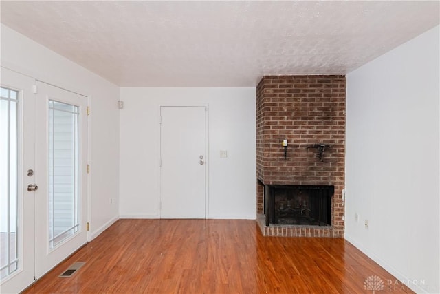 unfurnished living room with a textured ceiling, a brick fireplace, and wood-type flooring