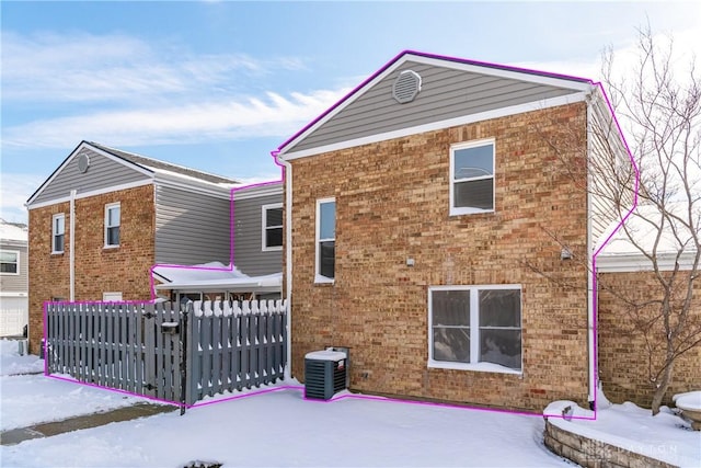 snow covered rear of property featuring central AC