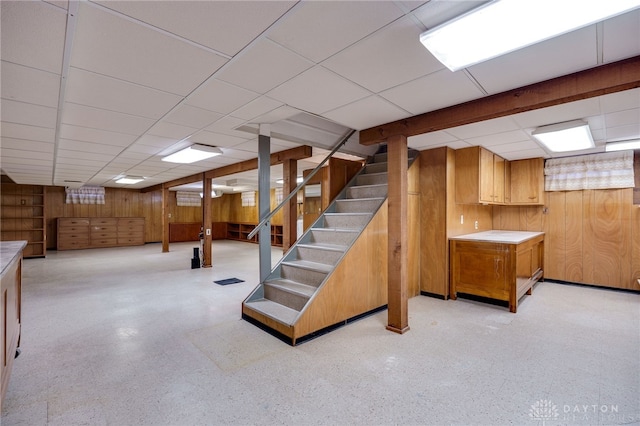 basement with a paneled ceiling and wood walls