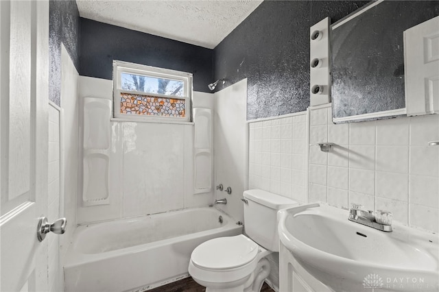 full bathroom featuring bathing tub / shower combination, toilet, a textured ceiling, tile walls, and vanity