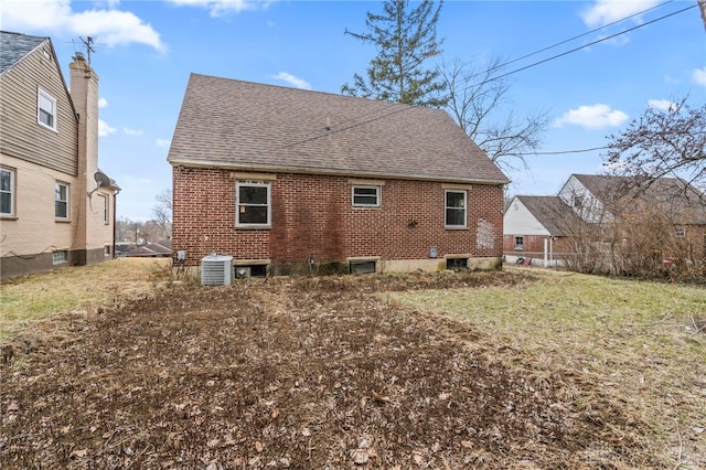 rear view of house with central AC unit and a lawn