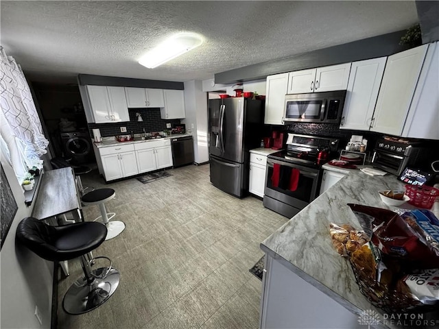 kitchen with appliances with stainless steel finishes, tasteful backsplash, washer / clothes dryer, sink, and white cabinetry