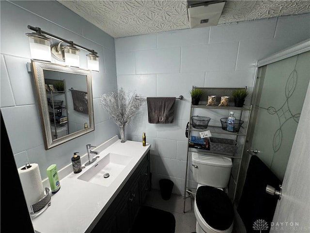 bathroom featuring tile walls, vanity, toilet, and a shower with shower door