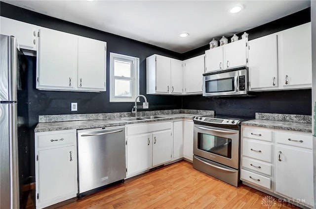 kitchen with sink, appliances with stainless steel finishes, white cabinets, and light hardwood / wood-style flooring