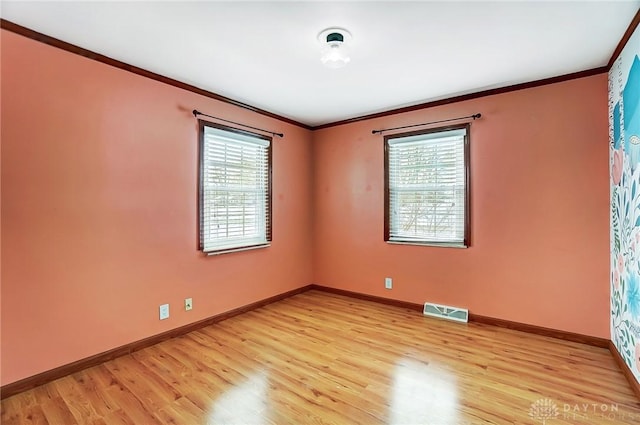 empty room with light hardwood / wood-style floors, a wealth of natural light, and ornamental molding