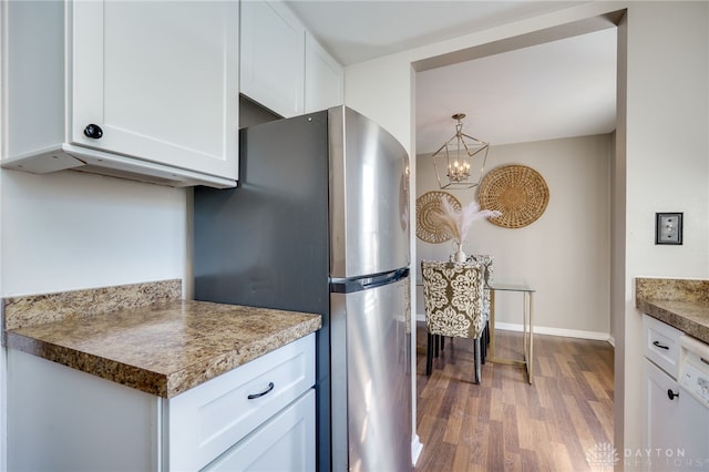 kitchen featuring decorative light fixtures, light wood finished floors, freestanding refrigerator, white cabinets, and baseboards