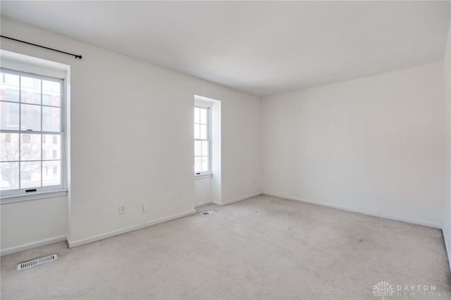 empty room with baseboards, visible vents, and light colored carpet