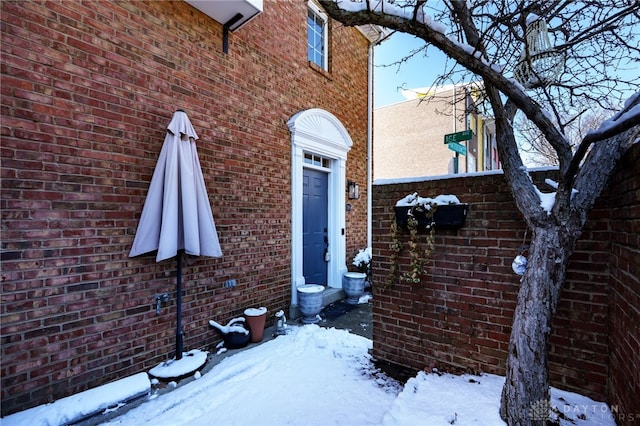 snow covered property entrance with brick siding