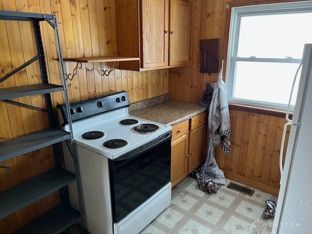 kitchen with electric stove, white fridge, and wood walls