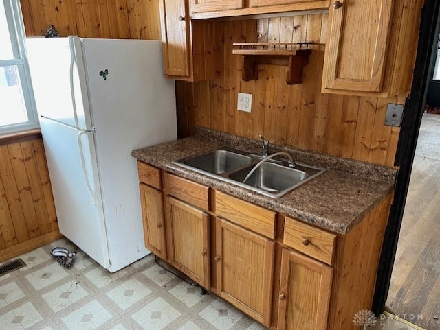 kitchen with white fridge, sink, and wood walls