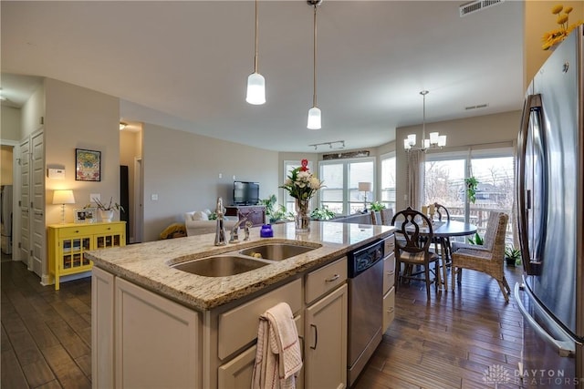 kitchen with appliances with stainless steel finishes, sink, light stone counters, hanging light fixtures, and an island with sink