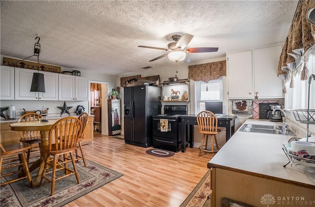 kitchen with light hardwood / wood-style flooring, white cabinets, black appliances, ceiling fan, and sink