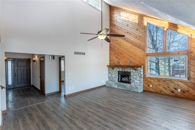 unfurnished living room with wooden walls, dark hardwood / wood-style flooring, a stone fireplace, and a high ceiling