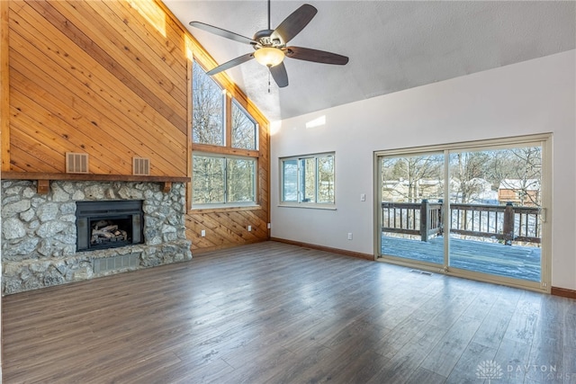 unfurnished living room with a healthy amount of sunlight, hardwood / wood-style flooring, a stone fireplace, and a textured ceiling