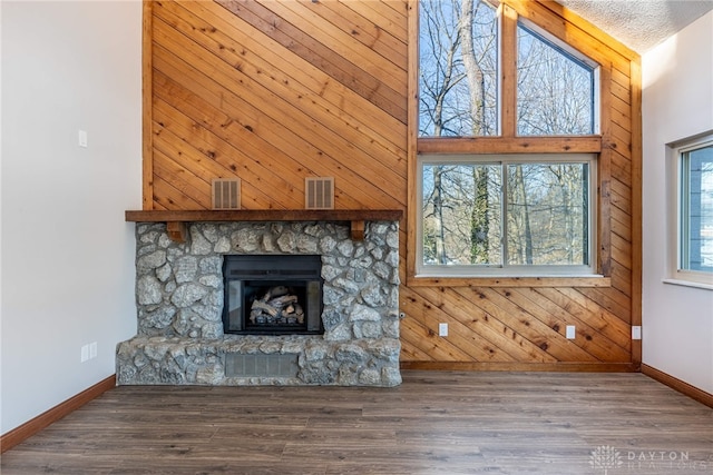 unfurnished living room with a fireplace, hardwood / wood-style flooring, a towering ceiling, and wooden walls