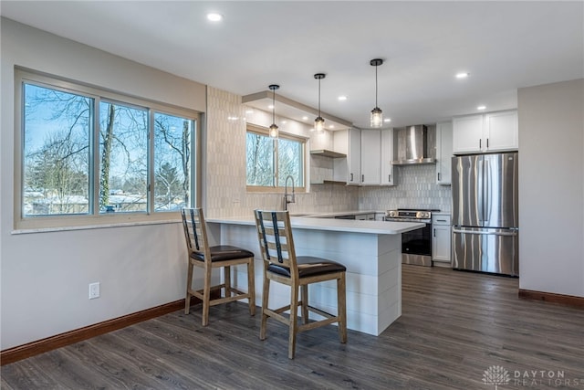 kitchen with appliances with stainless steel finishes, wall chimney range hood, kitchen peninsula, white cabinets, and hanging light fixtures