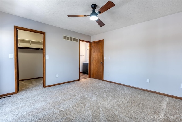 unfurnished bedroom featuring a textured ceiling, a spacious closet, light carpet, and a closet