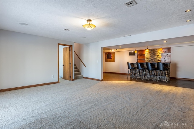 unfurnished living room featuring carpet, a textured ceiling, and bar area