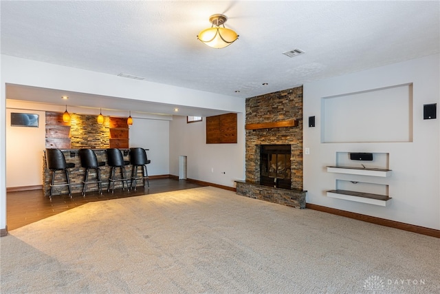 unfurnished living room featuring a stone fireplace, carpet floors, indoor bar, and a textured ceiling