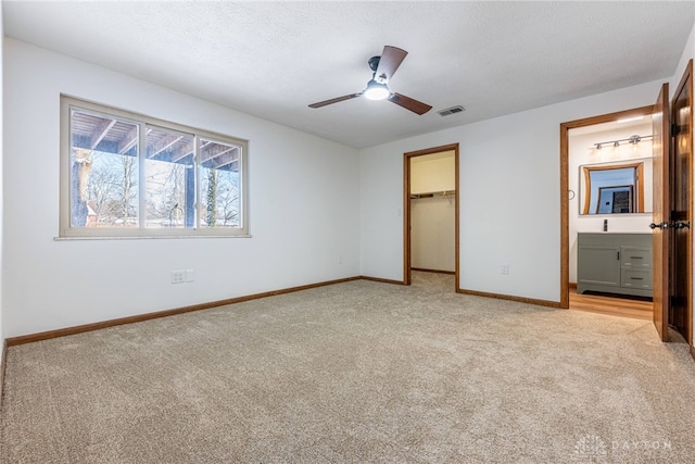 unfurnished bedroom with a closet, a spacious closet, a textured ceiling, connected bathroom, and light carpet