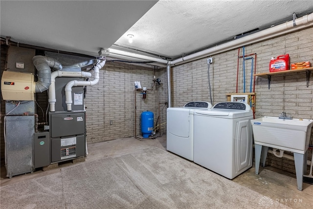 clothes washing area featuring heating unit, separate washer and dryer, a textured ceiling, and brick wall