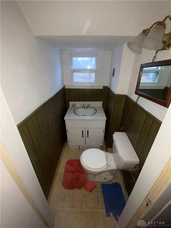 bathroom with toilet, vanity, tile patterned flooring, and wood walls